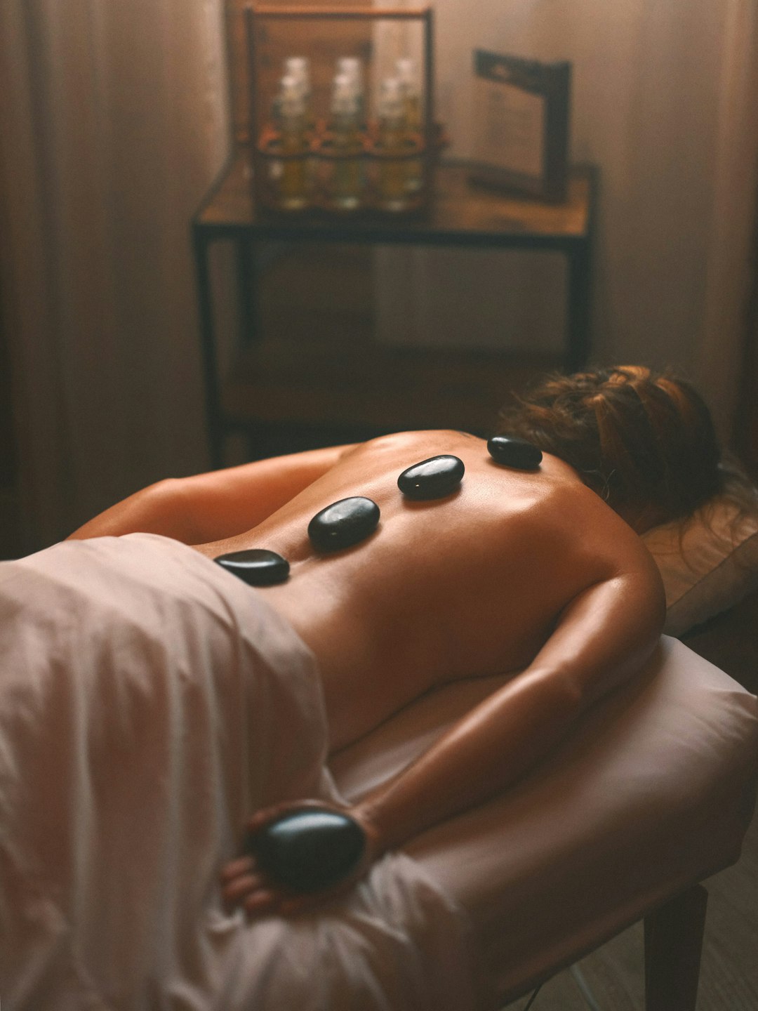 a-woman-laying-on-a-bed-with-hot-stones-on-her-back-tyra1ruaii